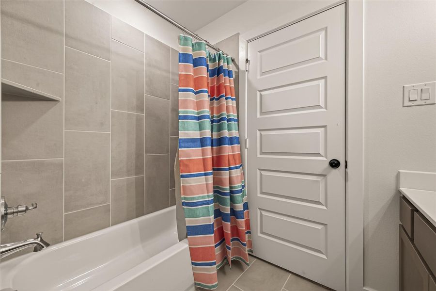 This bathroom features a contemporary design with a tiled shower and tub, a colorful striped shower curtain, and a paneled white door. The neutral tile flooring complements the sleek vanity.