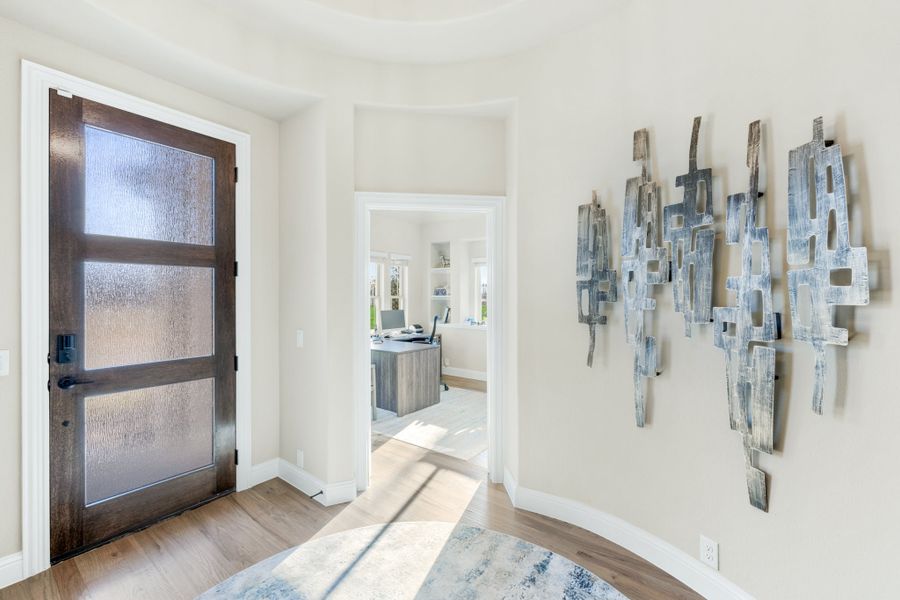 Foyer with dark wood front door with glass panels, metal wall art, and hardwood floors leading to a home office Foyer with dark wood front door with glass panels, metal wall art, and hardwood floors leading to a home office