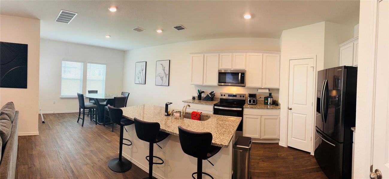 Kitchen featuring a granite island with seating, white cabinetry, recessed lighting, and wood-finish flooring Kitchen featuring a granite island with seating, white cabinetry, recessed lighting, and wood-finish flooring