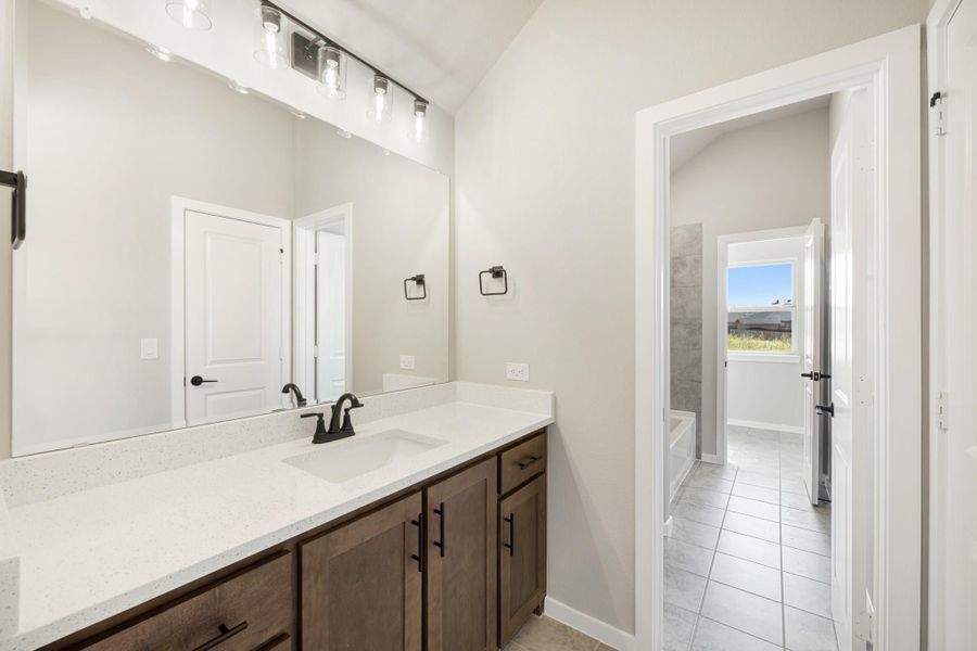 Bathroom vanity with dark wood cabinets, quartz countertop, single sink, and large mirror with overhead lighting