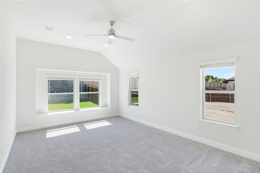 Empty bedroom with vaulted ceiling, ceiling fan, gray carpet, and multiple windows with backyard views