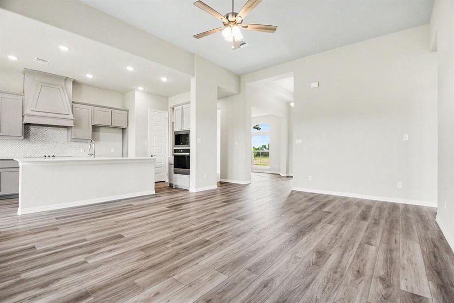 Kitchen and living area featuring wood-finish flooring, recessed lighting, ceiling fan, kitchen island with sink, and built-in double ovens Kitchen and living area featuring wood-finish flooring, recessed lighting, ceiling fan, kitchen island with sink, and built-in double ovens