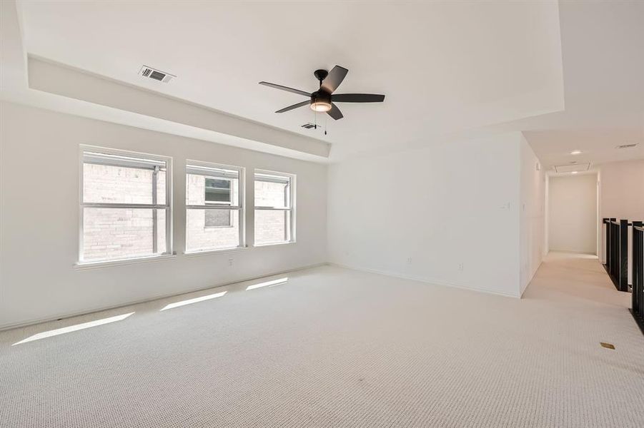 Unfurnished room featuring light carpet, a tray ceiling, and ceiling fan