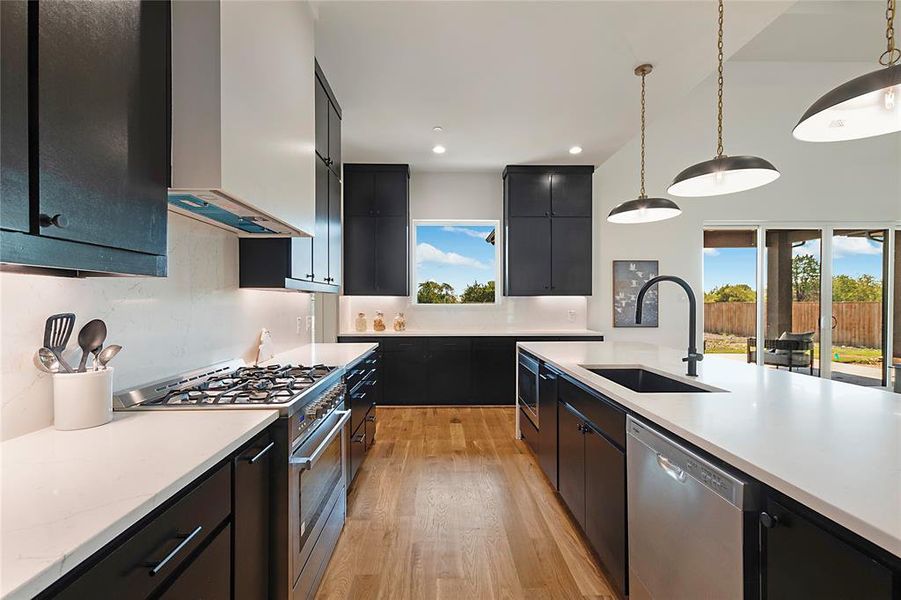 Contemporary kitchen featuring dark cabinetry, white countertops, and wood-finish flooring Contemporary kitchen featuring dark cabinetry, white countertops, and wood-finish flooring