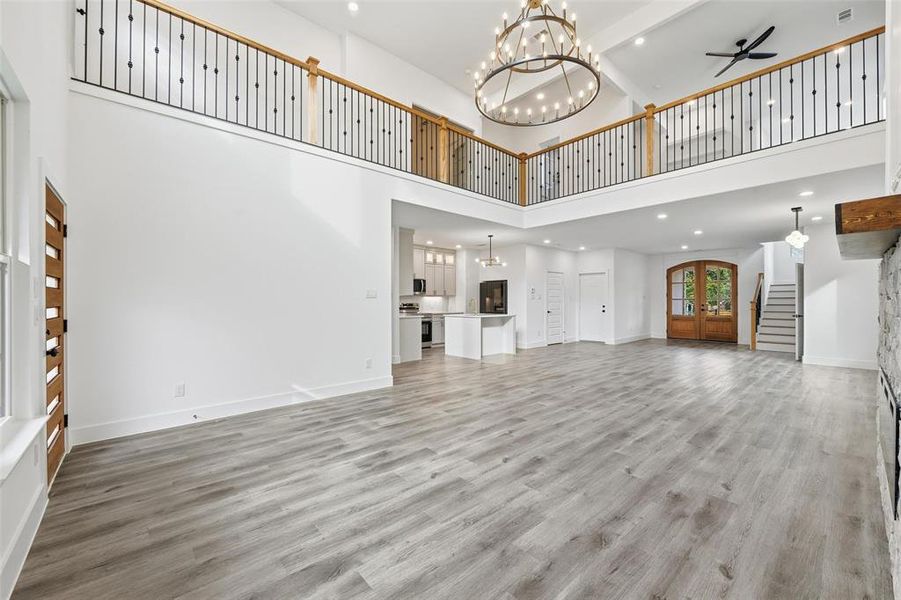 Unfurnished living room with a chandelier, stairway, light wood-style floors, recessed lighting, and a high ceiling