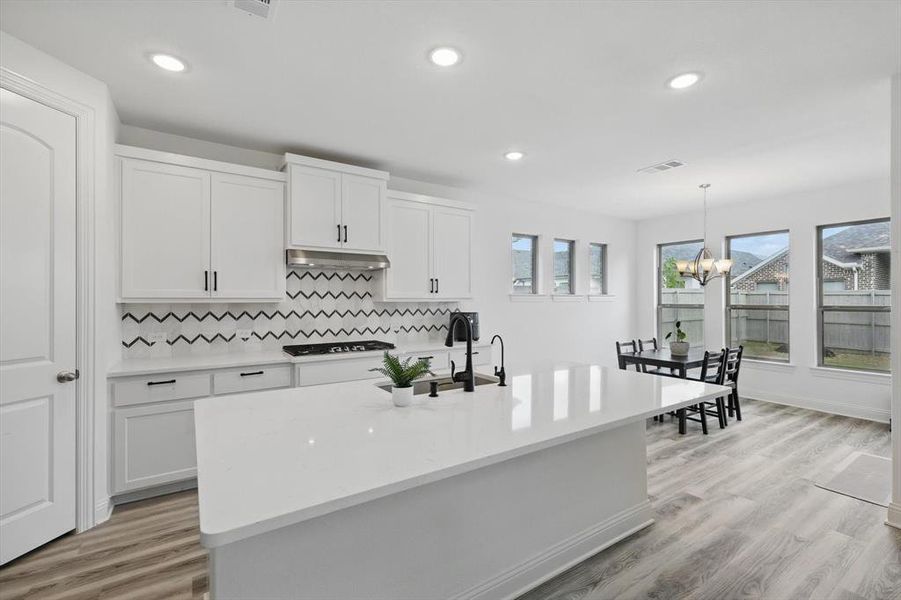 Kitchen with under cabinet range hood, light countertops, white cabinets, and cooktop