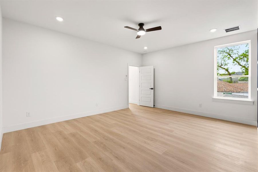 This room features light wood flooring, white walls, and a window providing natural light and views of green trees and rooftops