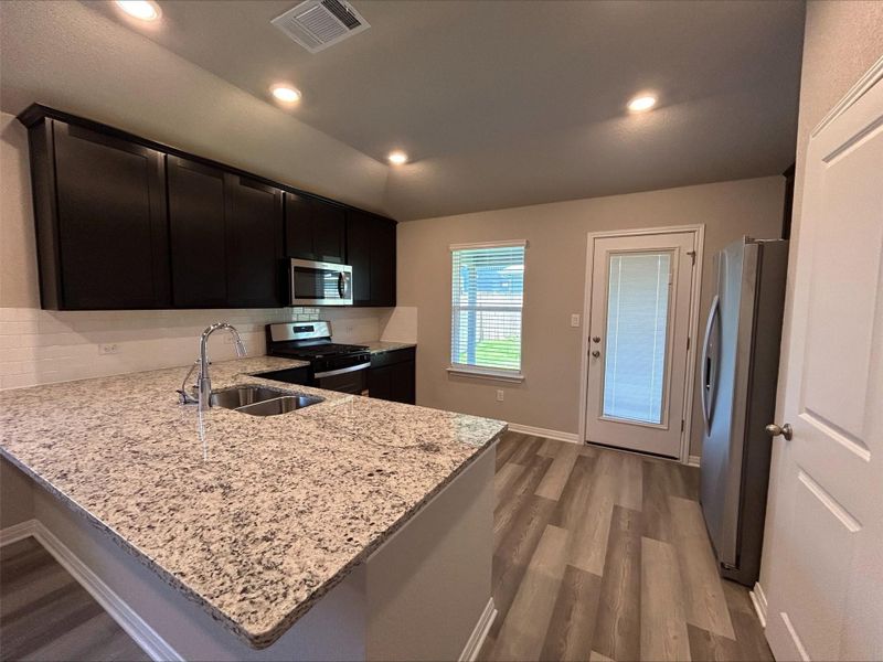 Kitchen featuring light wood-style floors, appliances with stainless steel finishes, light stone counters, a peninsula, and recessed lighting Kitchen featuring light wood-style floors, appliances with stainless steel finishes, light stone counters, a peninsula, and recessed lighting