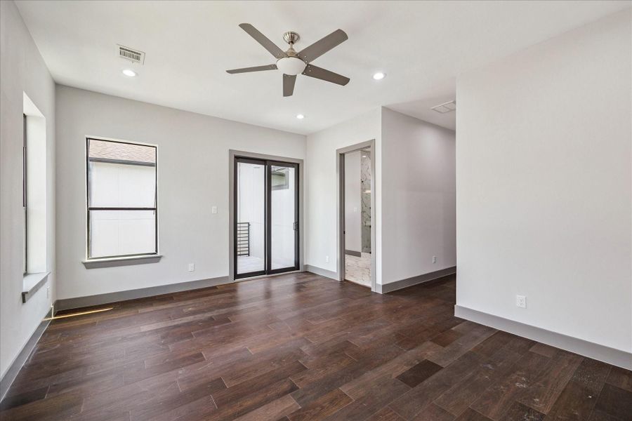 In the primary suite, elegant wood floors, recessed lighting, and a ceiling fan create comfort, while a sliding glass door opens to a private balcony and provides seamless entry to the en suite bathroom.