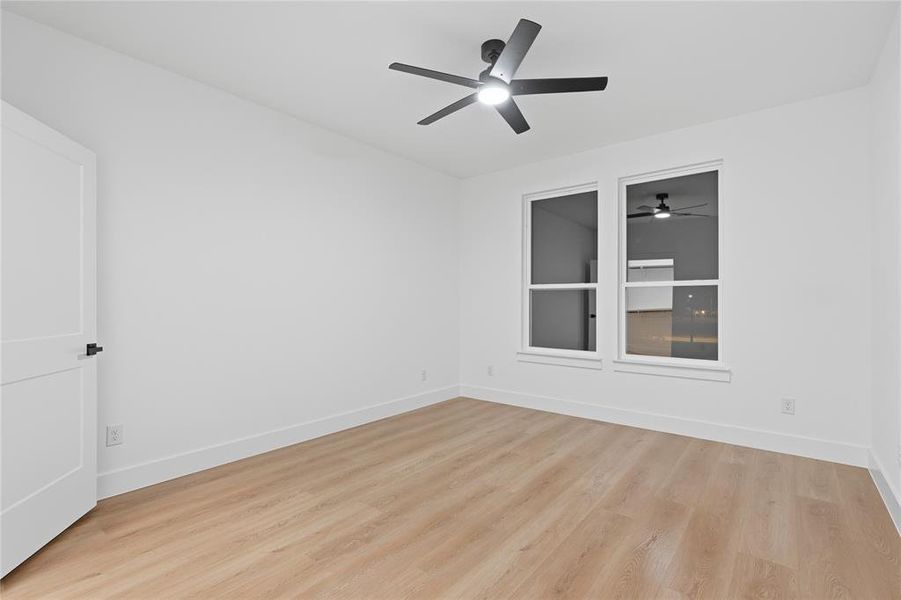 Bright room featuring two large windows, a ceiling fan with integrated lighting, wood-finish flooring, and a contemporary white door with matte black hardware Bright room featuring two large windows, a ceiling fan with integrated lighting, wood-finish flooring, and a contemporary white door with matte black hardware