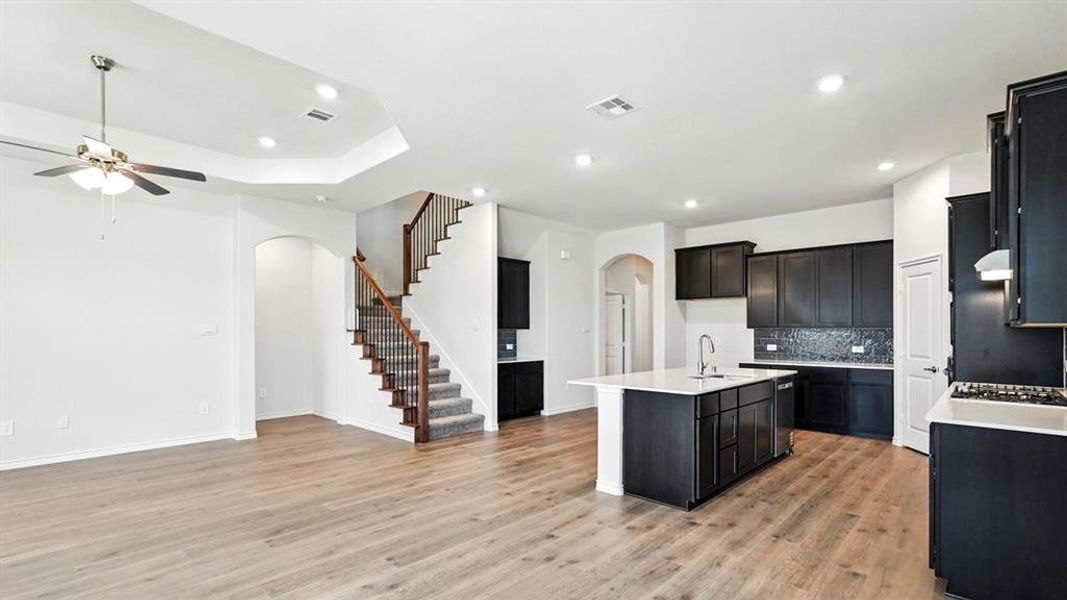 Kitchen with arched walkways, dark cabinetry, a center island with sink, open floor plan, and recessed lighting