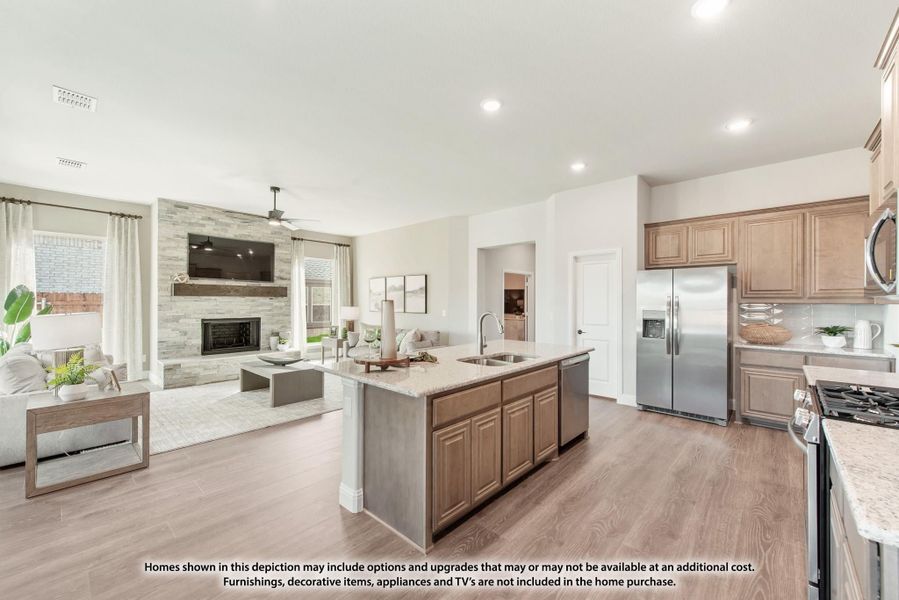 Open-concept kitchen with center island, wood cabinets, and stainless appliances flowing into living room with stone fireplace Open-concept kitchen with center island, wood cabinets, and stainless appliances flowing into living room with stone fireplace