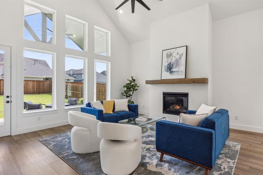 Living room with a tiled fireplace, hardwood / wood-style flooring, high vaulted ceiling, and ceiling fan