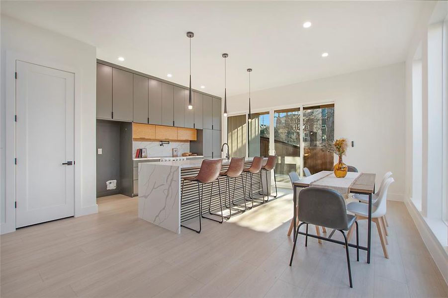 Kitchen featuring decorative backsplash, gray cabinetry, a breakfast bar, light hardwood / wood-style flooring, and hanging light fixtures