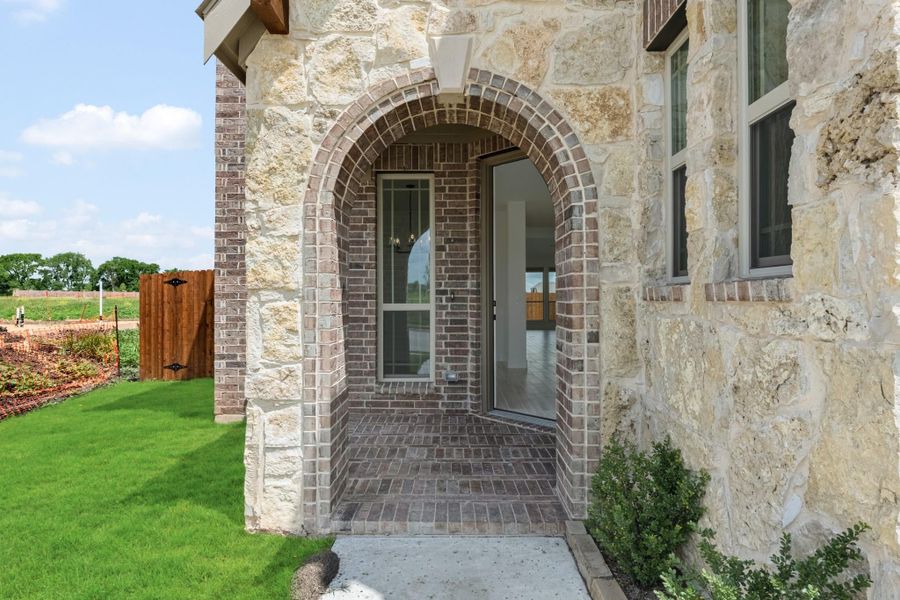 Home entrance with brick arched doorway, stone exterior walls, and brick paver porch Home entrance with brick arched doorway, stone exterior walls, and brick paver porch