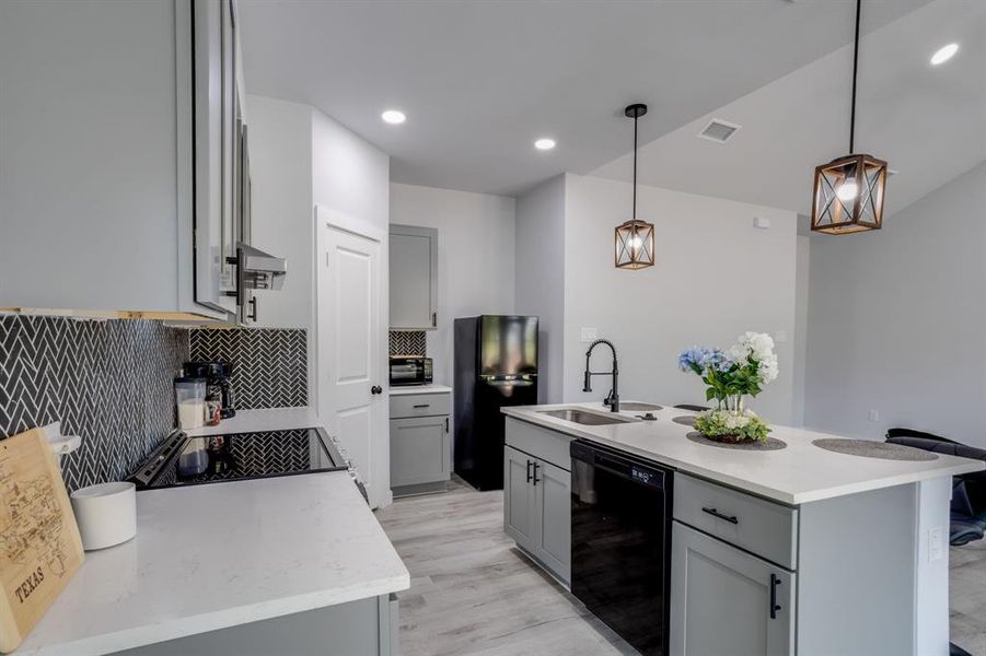 Kitchen with gray cabinets, backsplash, black appliances, an island with sink, and recessed lighting Kitchen with gray cabinets, backsplash, black appliances, an island with sink, and recessed lighting