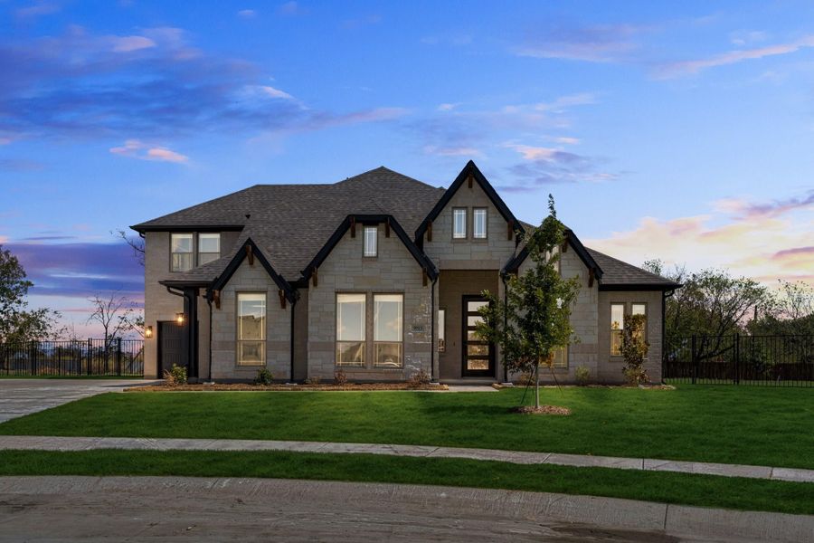 Two-story stone home with dark trim, steep roofline, and green front lawn at dusk