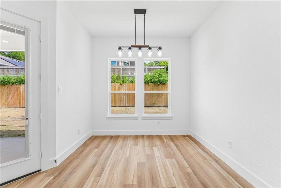 Room featuring wood-finish flooring, white walls, and a contemporary ceiling light fixture Room featuring wood-finish flooring, white walls, and a contemporary ceiling light fixture