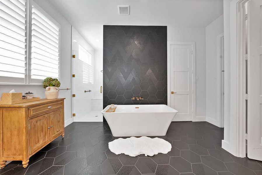 Freestanding soaking tub with brass fixtures set against a dark hexagonal tile accent wall Freestanding soaking tub with brass fixtures set against a dark hexagonal tile accent wall