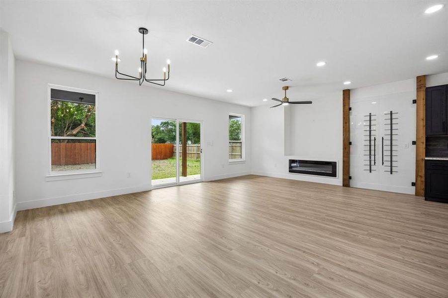 Open-concept living area featuring wood-finish flooring, a linear electric fireplace, and a contemporary chandelier Open-concept living area featuring wood-finish flooring, a linear electric fireplace, and a contemporary chandelier