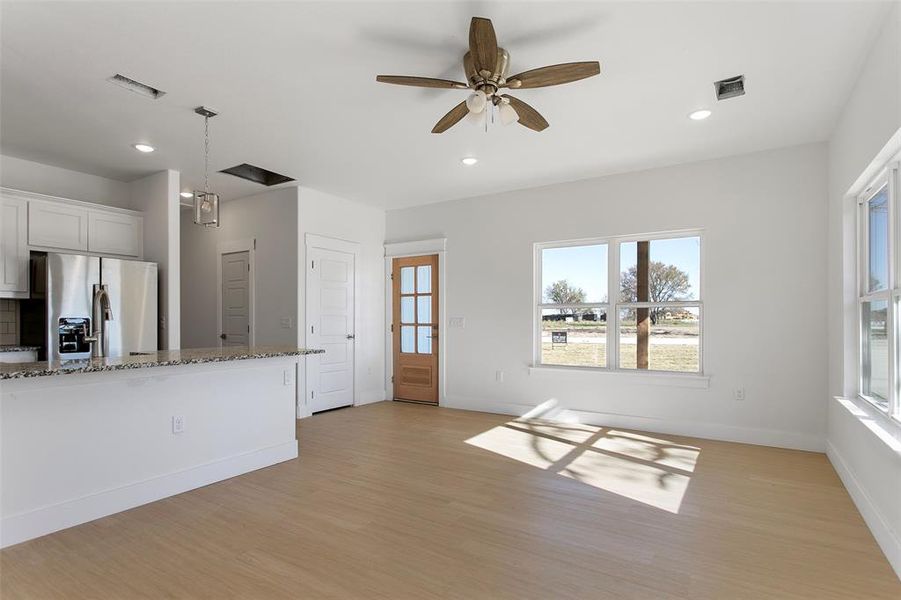 Kitchen featuring stainless steel fridge, white cabinets, a healthy amount of sunlight, and light stone counters