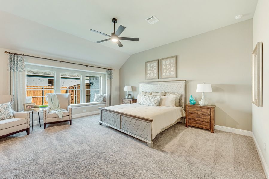 Spacious master bedroom with vaulted ceiling, ceiling fan, carpet floors, and large windows with seating area