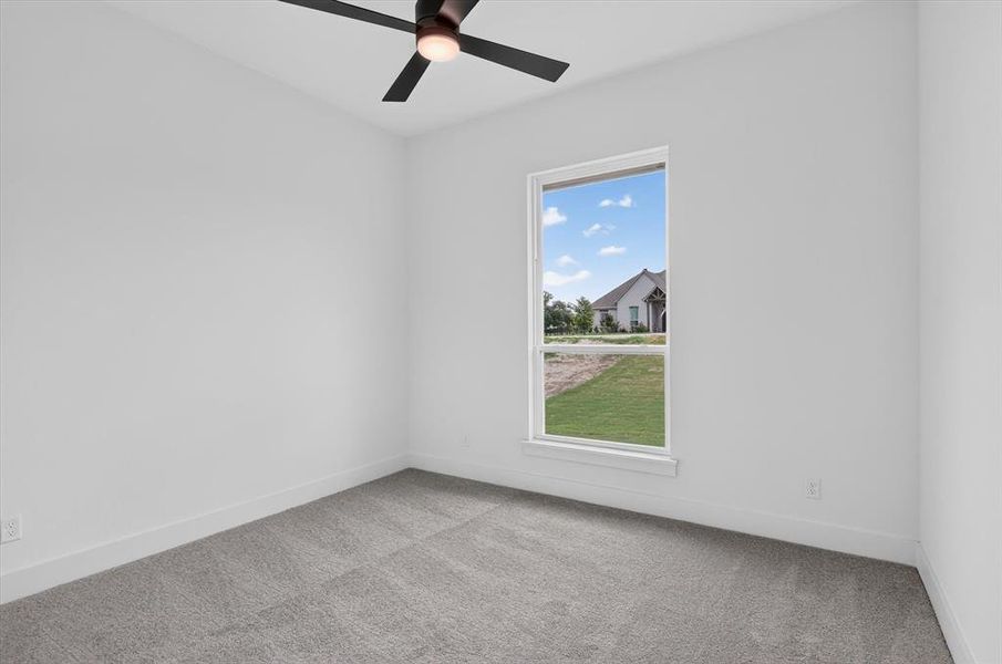 Carpeted room featuring a ceiling fan with integrated lighting, a large window, white baseboards, and neutral wall tones Carpeted room featuring a ceiling fan with integrated lighting, a large window, white baseboards, and neutral wall tones
