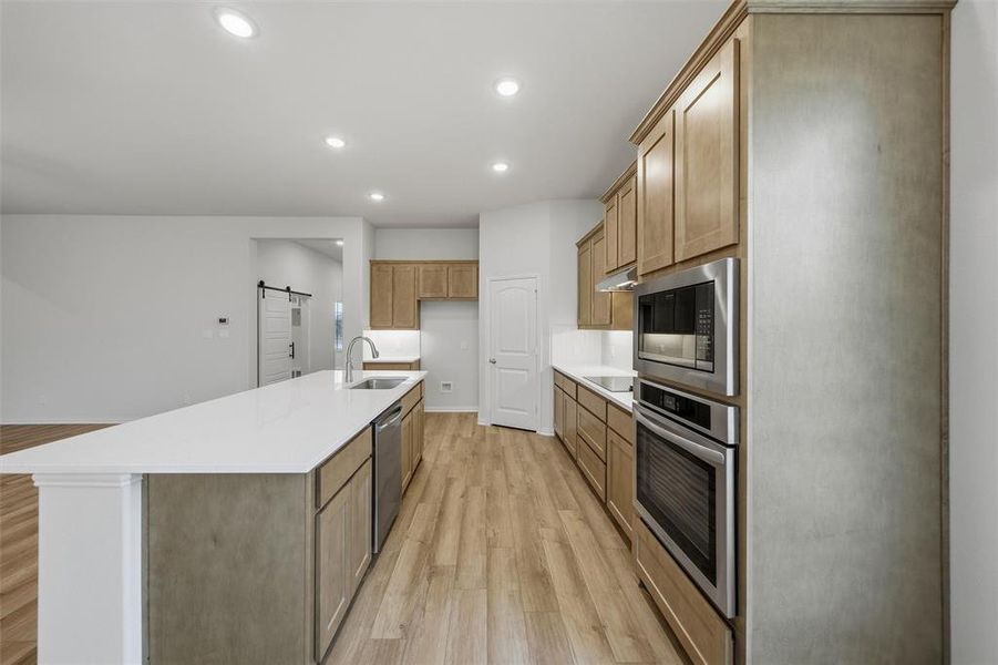 Kitchen with light wood-type flooring, stainless steel appliances, recessed lighting, a barn door, and an island with sink Kitchen with light wood-type flooring, stainless steel appliances, recessed lighting, a barn door, and an island with sink