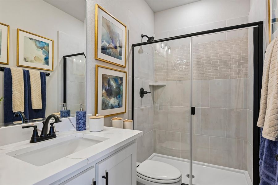 Bathroom with white vanity, black fixtures, glass-enclosed tile shower, and framed wall art Bathroom with white vanity, black fixtures, glass-enclosed tile shower, and framed wall art