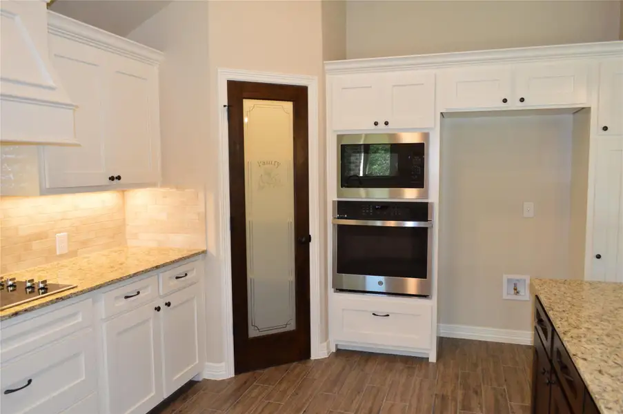 Kitchen featuring appliances with stainless steel finishes, custom range hood, tasteful backsplash, and wood tiled floors