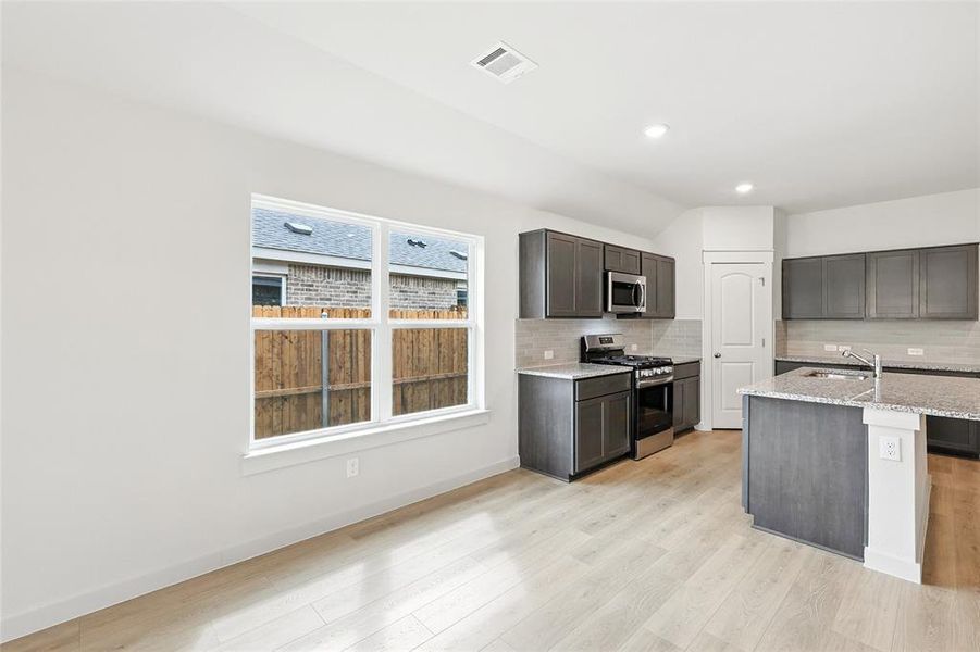 Kitchen featuring stainless steel appliances, decorative backsplash, light wood-style floors, light stone countertops, and recessed lighting