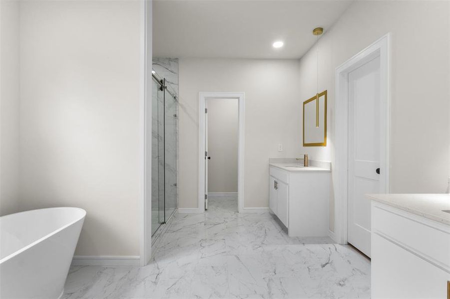 Spacious bathroom featuring a freestanding soaking tub, a walk-in shower with a glass enclosure and tiled surround, dual vanity areas with white cabinetry and light countertops, and large format marble-look floor tiling