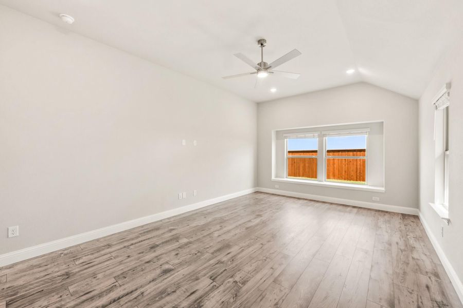 Empty room with vaulted ceiling, ceiling fan, hardwood floors, and a backyard-facing window Empty room with vaulted ceiling, ceiling fan, hardwood floors, and a backyard-facing window