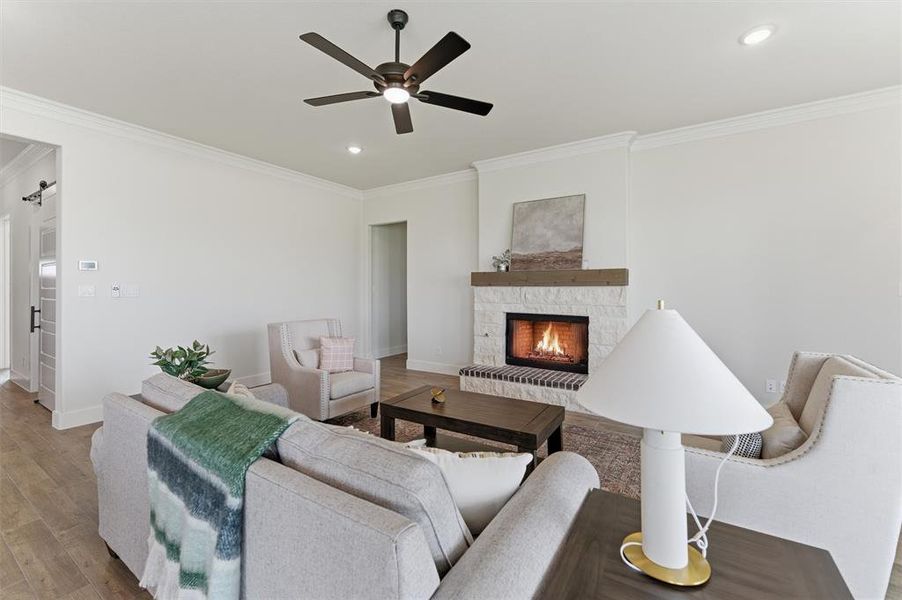 Living area featuring a stone-clad fireplace with a wood mantel, wood-finish flooring, recessed lighting, crown molding, and a ceiling fan