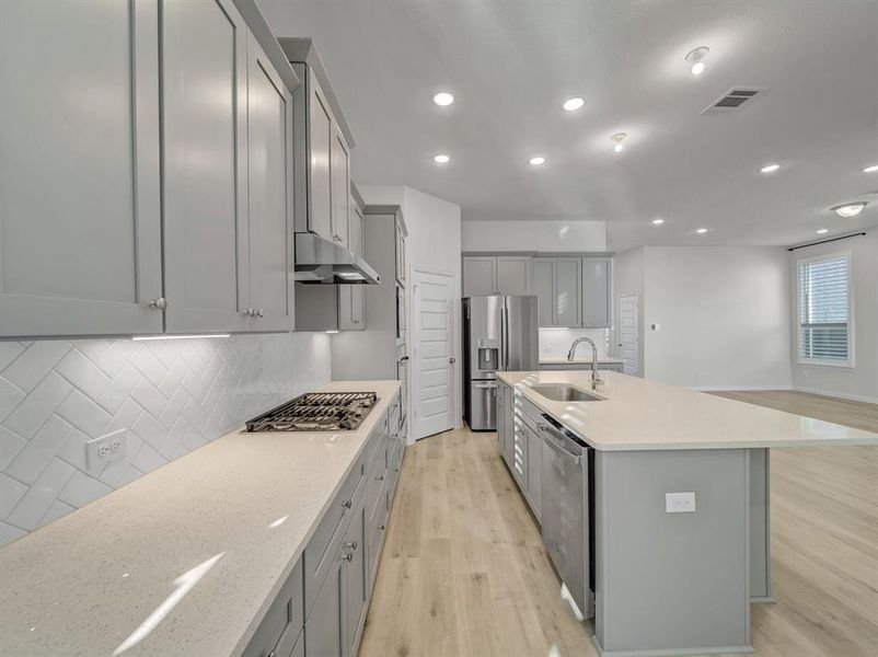 Kitchen with a kitchen island with sink, sink, light hardwood / wood-style flooring, appliances with stainless steel finishes, and tasteful backsplash