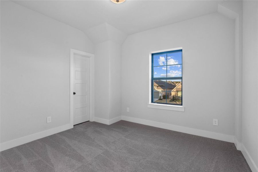 This secondary bedroom offers plush carpeting, neutral paint tones, lighting, a large window, and walk-in closet.