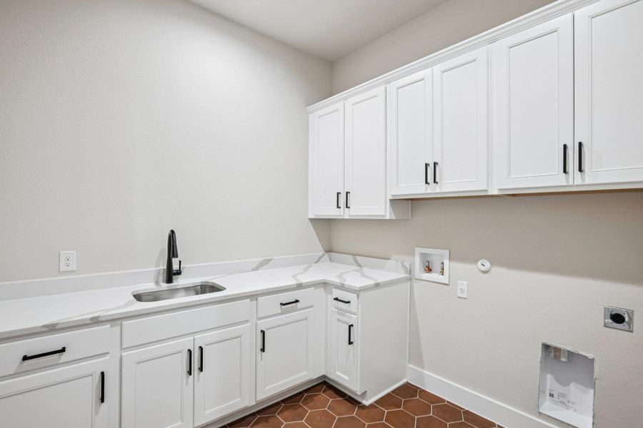 Washroom with hookup for a gas dryer, hookup for a washing machine, cabinet space, hookup for an electric dryer, and dark tile patterned floors