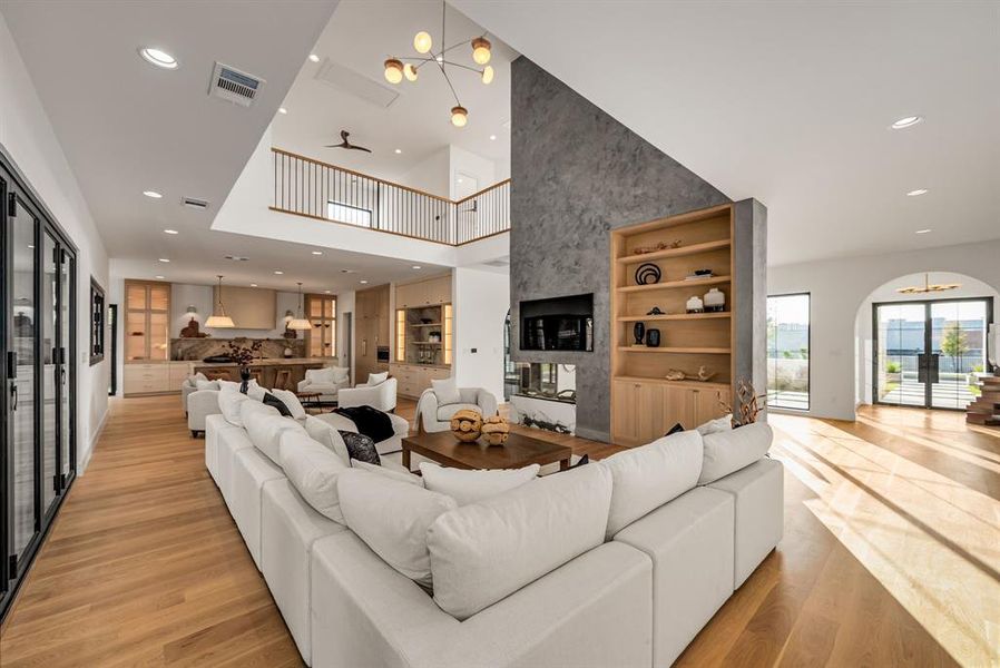 Living room featuring recessed lighting, light wood-style flooring, a high ceiling, built in features, and arched walkways Living room featuring recessed lighting, light wood-style flooring, a high ceiling, built in features, and arched walkways