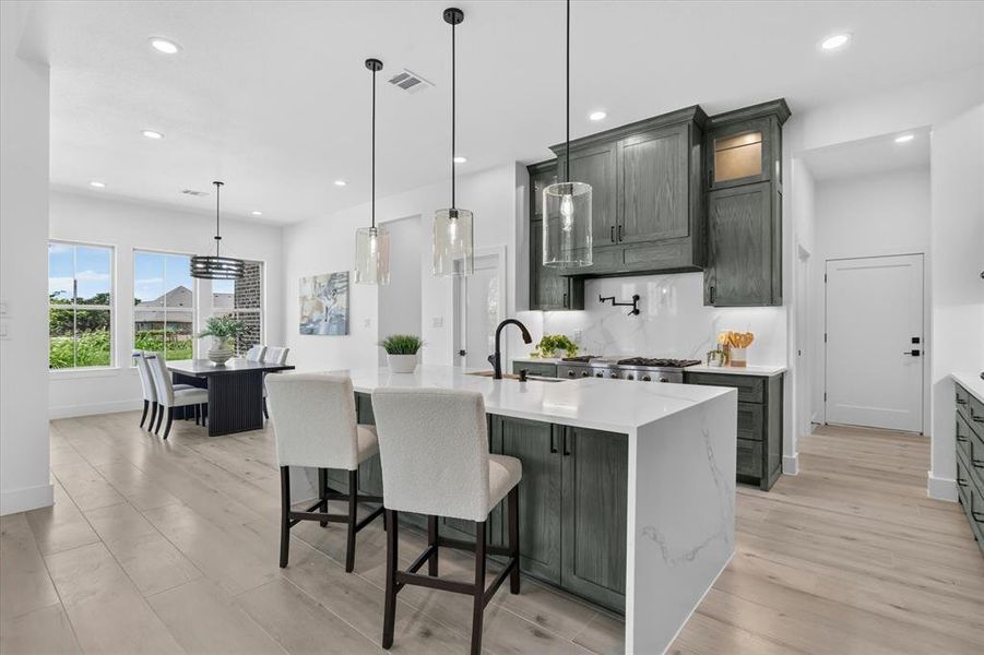 Open-concept kitchen and dining area featuring a waterfall-edge island with seating, a gas range with a tile backsplash, wood-finish flooring, and ample natural light from multiple windows