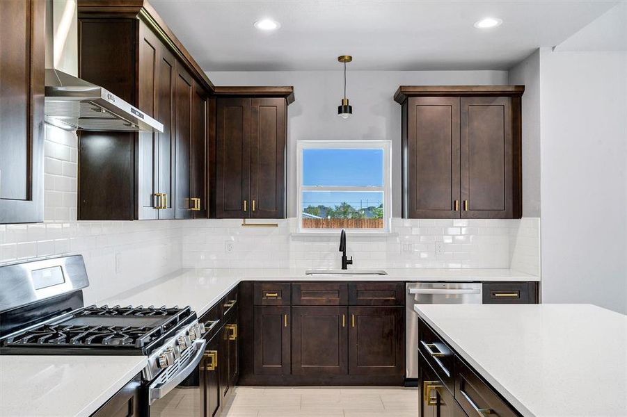 Kitchen with hanging light fixtures, sink, wall chimney exhaust hood, appliances with stainless steel finishes, and tasteful backsplash