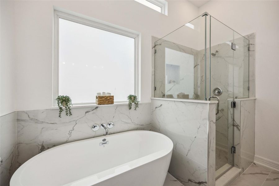 This spa-inspired primary bath is equipped with a double vanity, a deep soaking tub, and a separate glass-enclosed shower. High-end quartzite finishes and soft-close cabinetry carry the luxury aesthetic throughout.