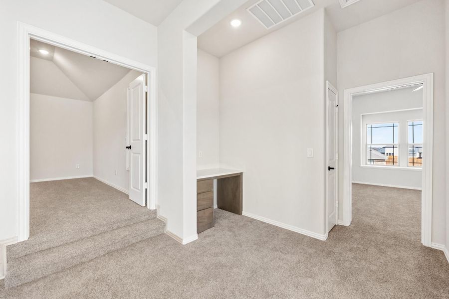 Upstairs hallway with built-in desk, gray carpet, and doors leading to bedroom and walk-in closet