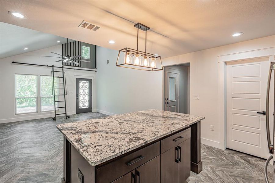 Kitchen featuring dark brown cabinets, recessed lighting, a kitchen island, light stone counters, and pendant lighting Kitchen featuring dark brown cabinets, recessed lighting, a kitchen island, light stone counters, and pendant lighting