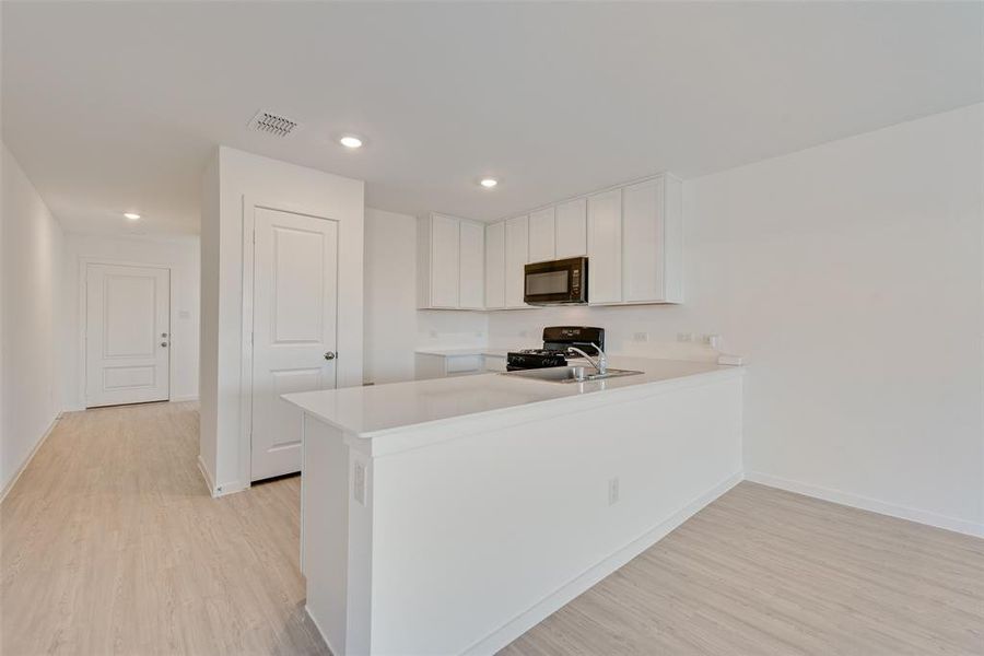 Kitchen featuring white cabinetry, light hardwood / wood-style flooring, black appliances, and kitchen peninsula