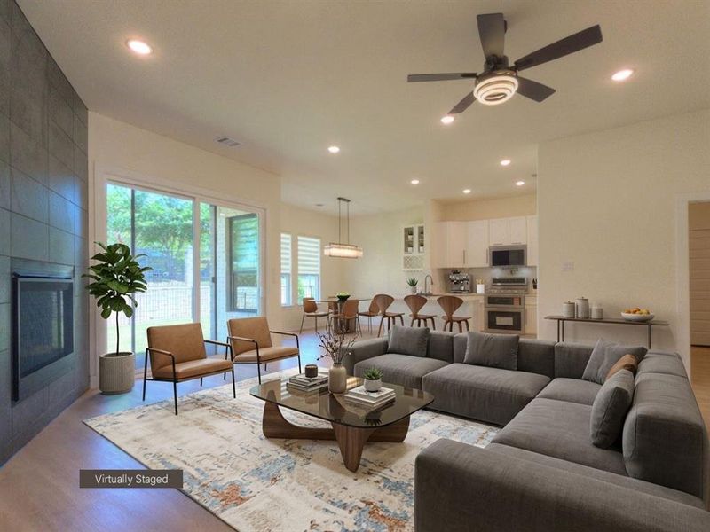 Expansive open-concept living area featuring wood-finish flooring, a contemporary fireplace with a full-height tiled surround, and recessed lighting