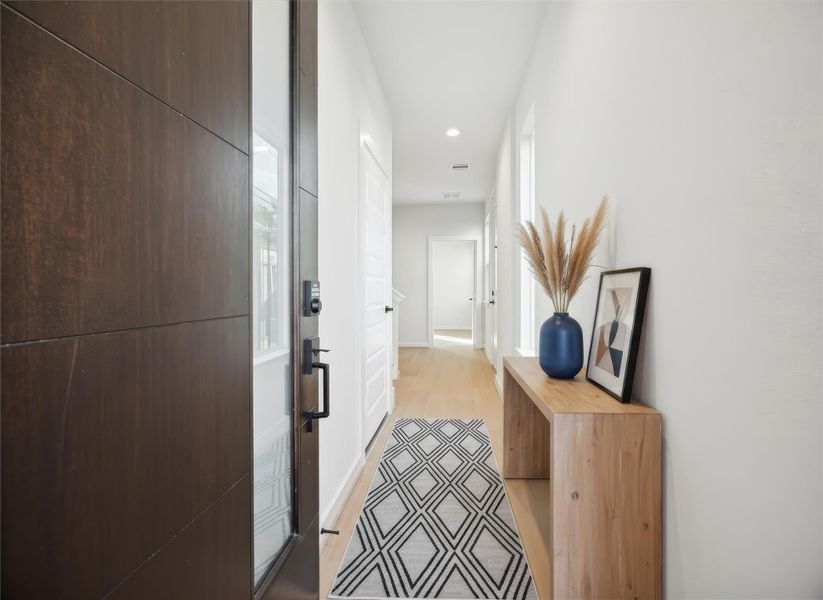 Entryway features a modern aesthetic with LVP light oak–style floors and crisp white trim for a clean, welcoming feel. The open staircase leads to the upper level, and just beyond it, an entry to a guest suite/flex space adds convenience and versatility to the layout. *Virtually staged*