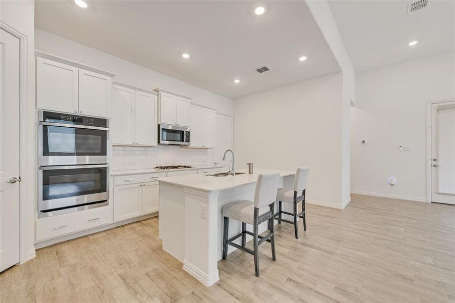 Kitchen featuring appliances with stainless steel finishes, an island with sink, tasteful backsplash, light wood-style floors, and a kitchen breakfast bar Kitchen featuring appliances with stainless steel finishes, an island with sink, tasteful backsplash, light wood-style floors, and a kitchen breakfast bar