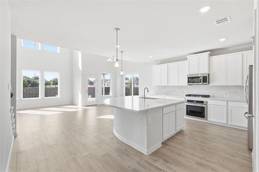Kitchen with hanging light fixtures, white cabinetry, backsplash, open floor plan, and recessed lighting