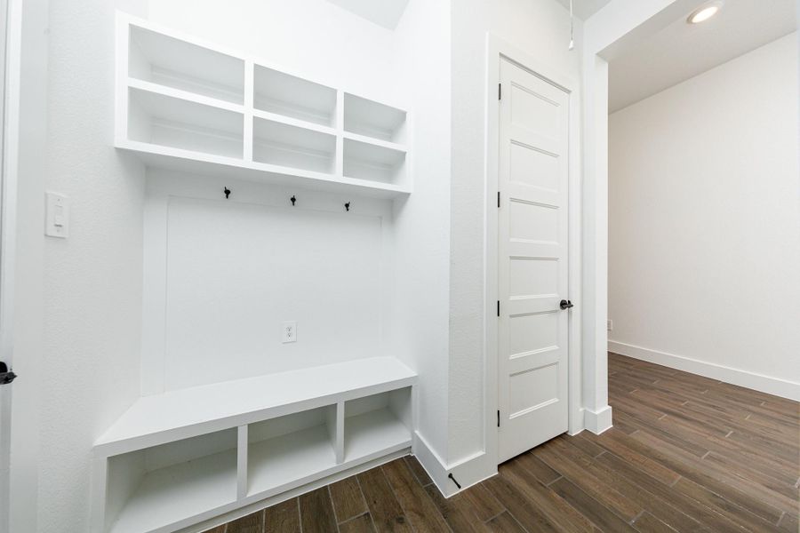 Step into this highly functional and stylish mudroom drop zone, an essential feature for a busy household. The space boasts custom-built white cabinetry and shelving, providing generous storage for coats, bags, and shoes. A comfortable built-in bench offers a convenient spot to sit, while three sleek hooks keep outerwear tidy and accessible.