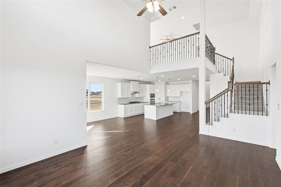 Spacious interior featuring soaring vaulted ceilings, dark wood-finish flooring, a contemporary kitchen with white cabinetry and a central island, and a dual-level staircase with wrought iron balusters